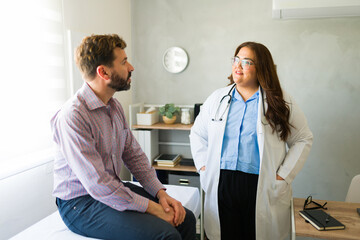 Fototapeta premium Confident female doctor having conversation with patient during medical consultation in doctor's office