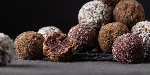 Assortment of gourmet handcrafted vegan chocolate truffle candies on dark background from premium confectionary. Bited handmade bonbon chocolatier concept. Horizontal banner with copy space