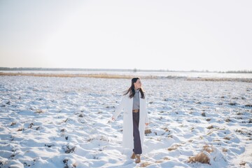 Happy young woman walking on snow covered meadow in winter sunny day.