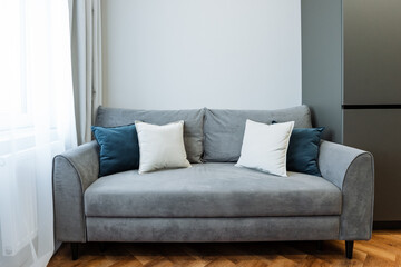 In a cozy and inviting living room, a chic grey couch adorned with vibrant blue and white throw pillows beautifully enhances the overall design, atmosphere, and ambiance of the space
