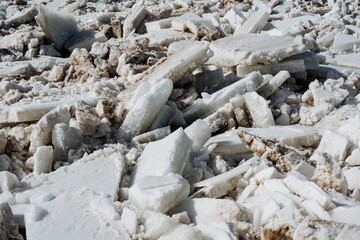 A large, uneven pile of broken pieces of ice lies scattered across the ground, creating a striking and unusual sight that naturally captures the attention of curious passersby nearby