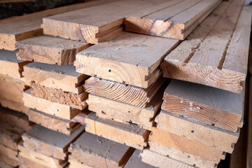 Stacked lumber. Folded wood.Closeup wooden boards.The surface of the end of the board.Lots of planks stacked on top of each other in the warehouse. White Pine decking planks heap - side view.
