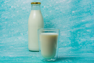 Full glass of milk sits next to a glass milk bottle on a blue surface. Scene evokes freshness and simplicity, perfect for dairy, breakfast, and healthy lifestyle themes.