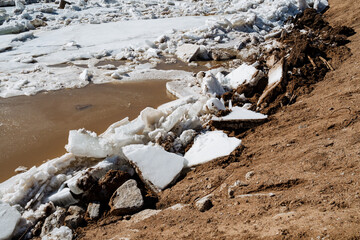 A large pile of ice is resting on the ground adjacent to a body of water, presenting a fascinating view of natures beauty and the transition between solid and liquid states