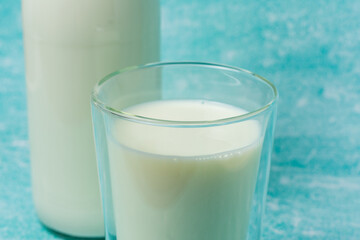 Full glass of milk sits next to a glass milk bottle on a blue surface. Scene evokes freshness and simplicity, perfect for dairy, breakfast, and healthy lifestyle themes.
