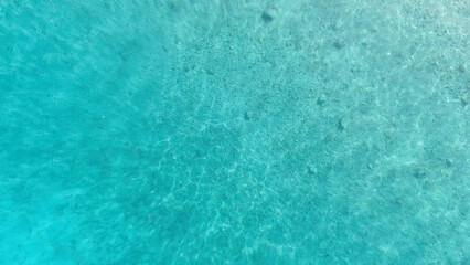 Drone view of the transparent turquoise waters of the Adriatic Sea shimmering under the sun. The seabed with visible stones adds depth and natural beauty, perfect for travel and nature themes.
