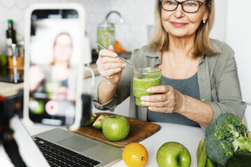 Selective focus on mature female blogger influencer nutritionist in glasses sharing recipe of fresh...