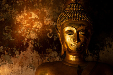 Gold buddha statue in front of the old wall background at Thai temple.