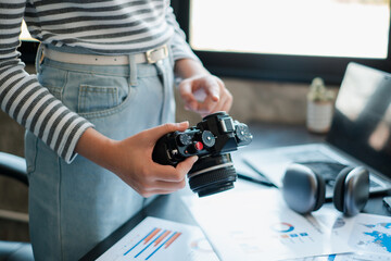A person examines photos on a digital camera in a contemporary office setting, surrounded by charts and headphones.