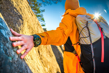 Close-up of hiker’s hand touching rock, wearing orange jacket and wristwatch