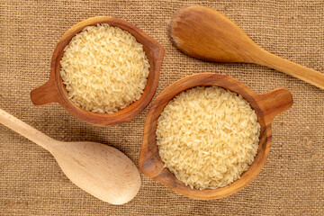 Steamed raw rice in wooden cups with wooden spoons on jute cloth, close-up, top view.