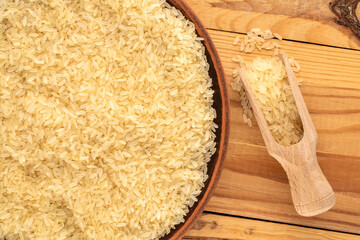 Steamed raw rice with a clay plate and a wooden spoon on a wooden table, close-up, top view.