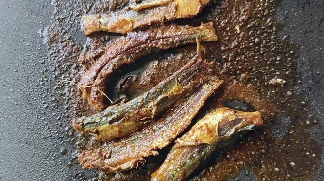 small fish being fried in oil on a pan. The fish have a crispy, golden-brown texture with a slightly charred appearance