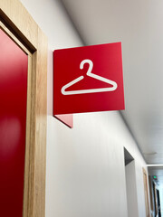 Red sign with a white hanger icon marks a changing room or wardrobe area in a modern public hallway.