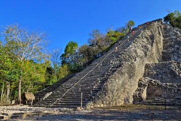 Old mayan temple with tourists under the blue sky. Ancient pyramid and green vegetation. Mexican remains of mayan civilization.