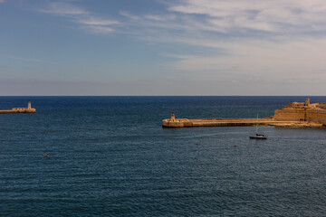 Lighthouses at Grand Harbour, Malta. Scenic view of the blue Mediterranean Sea, historic stone pier, and red and green lighthouses marking the entrance to Valletta’s Grand Harbour.