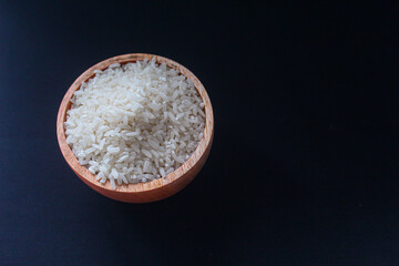 Zakat fitrah concept: Wooden bowl filled with rice on a black background.