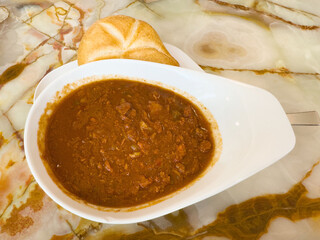 Rich beef stew with bread roll on marble table