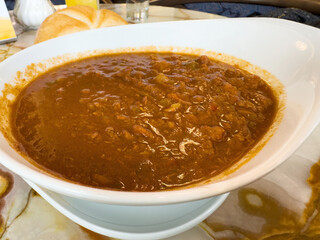 Spicy beef goulash in a white bowl with bread on marble table