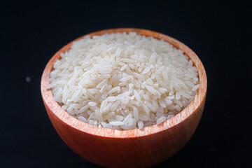 Zakat fitrah concept: Wooden bowl filled with rice on a black background.