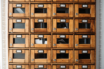 Vintage wooden mailbox wall with numbered glass-front compartments, symbolizing analog communication and architectural nostalgia. Retro design, analog revival, organizational systems.