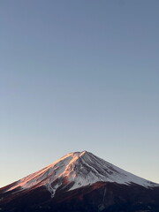 Fototapeta premium A stunning view of Mount Fuji at sunrise with golden sunlight illuminating the snow-capped peak, set against a clear blue sky in Yamanashi Prefecture, Japan.