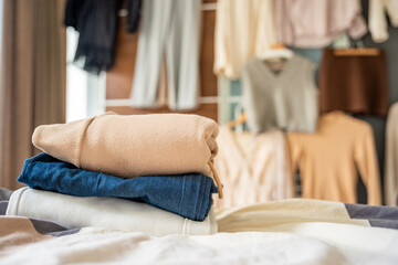 Stacked pile of clothing prepared for resale, donation, or recycling, with wardrobe with outfits in...