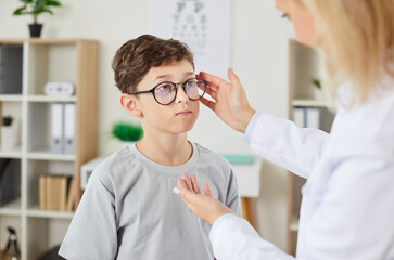 Doctor ophthalmologist assists a child patient with eyeglasses prescription during an eye exam at...