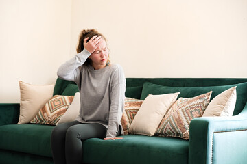 A young woman having a headache sitting on a couch at home. Girl holding her head in pain. Vertigo...