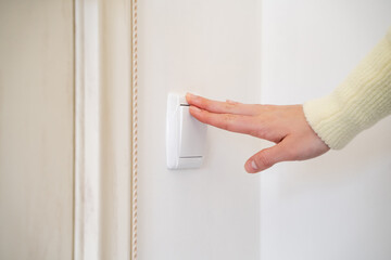 A female hand pressing a white plastic light switch buttons on a wall in room close up. The young...