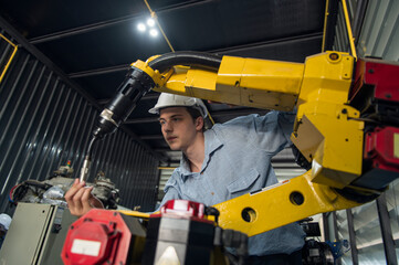 Engineer standing by robotic arm and operating machine in industry factory, technician worker check for repair maintenance electronic operation