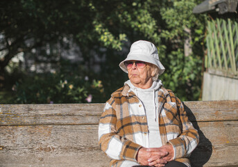 Stylish Senior woman 90 years old in a white panama hat and sunglasses on a walk in the summer,
