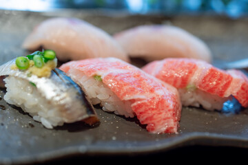 Nigiri sushi with fresh fatty tuna and mackerel garnished with green onions and grated ginger served on a black ceramic plate in a Japanese restaurant with soft lighting