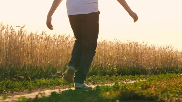 Unrecognizable boy teenager running on dirt road at natural sunlight autumn summer field back view closeup. Happy male teen relaxing outdoor enjoy freedom leisure activity sunny meadow sky landscape