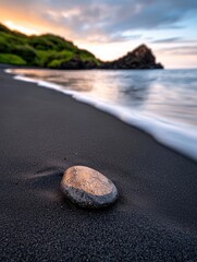 Obraz premium A serene beach scene featuring a smooth stone on dark sand with gentle waves lapping at the shore.