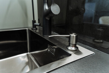 This is a stainless steel kitchen sink that features a sleek black faucet as well as a convenient soap dispenser designed for ease of use and aesthetic appeal in the kitchen