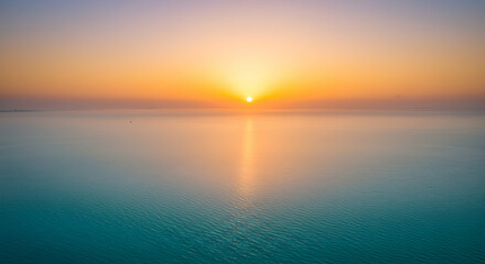 Obraz premium Ocean Sunset with Orange Sky Reflection Over Calm Blue Water