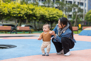 Mother helping baby learn to walk outdoors
