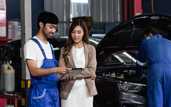 Handsome male mechanic wearing uniform, using tablet, checking or inspecting for fix, repair car or automobile components, talking with customer, working in car maintenance service center or shop.