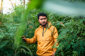 A man wearing a yellow jacket explores a lush green forest, surrounded by dense vegetation and...