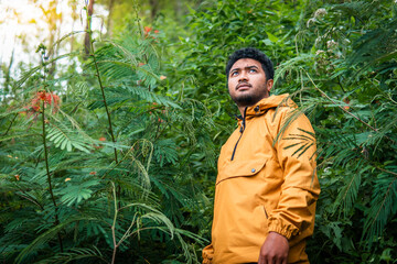 A man wearing a yellow jacket explores a lush green forest, surrounded by dense vegetation and...