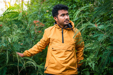 A man wearing a yellow jacket explores a lush green forest, surrounded by dense vegetation and...