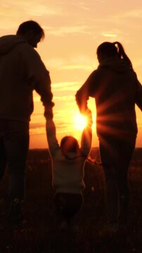 Silhouettes of having fun mom dad kid. Golden sunset, cheerful joyful family at holidays holding hands, lifting baby girl high in air, playing together. Fun active game. Traveling by car to nature.
