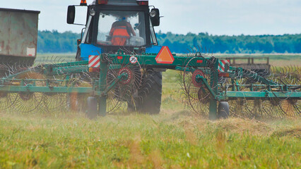 Heavy duty tractor raking freshly cut grass, sunlight glinting on metal, transforming green field...
