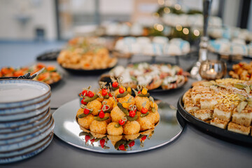 Close-up of assorted savory appetizers and desserts on a catering table with plates stacked nearby at an indoor event or celebration..