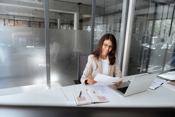Latin business woman saleswoman working on laptop computer reading financial bank document in office workplace. Young entrepreneur manager businesswoman specialist doing paperwork using pc. Copy space