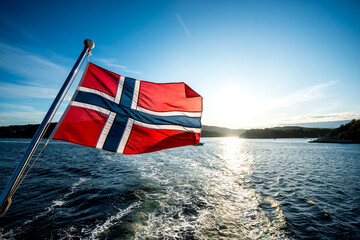 Norwegian flag on a ship or boat with the Oslo fjord in Norway in the background, sightseeing ferry