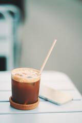 Close-up of iced espresso tonic with foam in glass on cork coaster with eco-friendly straw,...