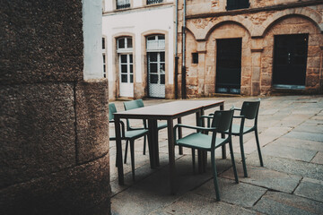 Modern outdoor dining setup in Spain with green chairs and rectangular table in cozy historic European courtyard surrounded by textured stone buildings, Santiago de Compostela