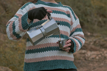 Woman with an Italian coffee maker and a thermal aluminum cup in the middle of a forest, woman camping drinking coffee